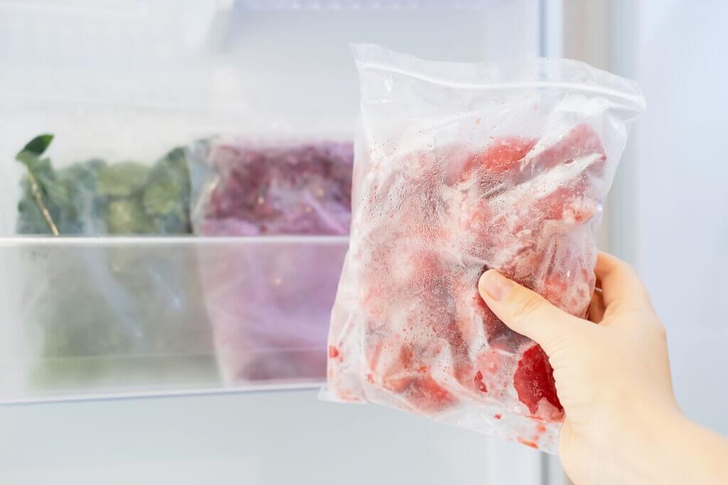 Female hand holds a plastic bag with a zip fastener with frozen strawberries against the background of an open with other vegetables.