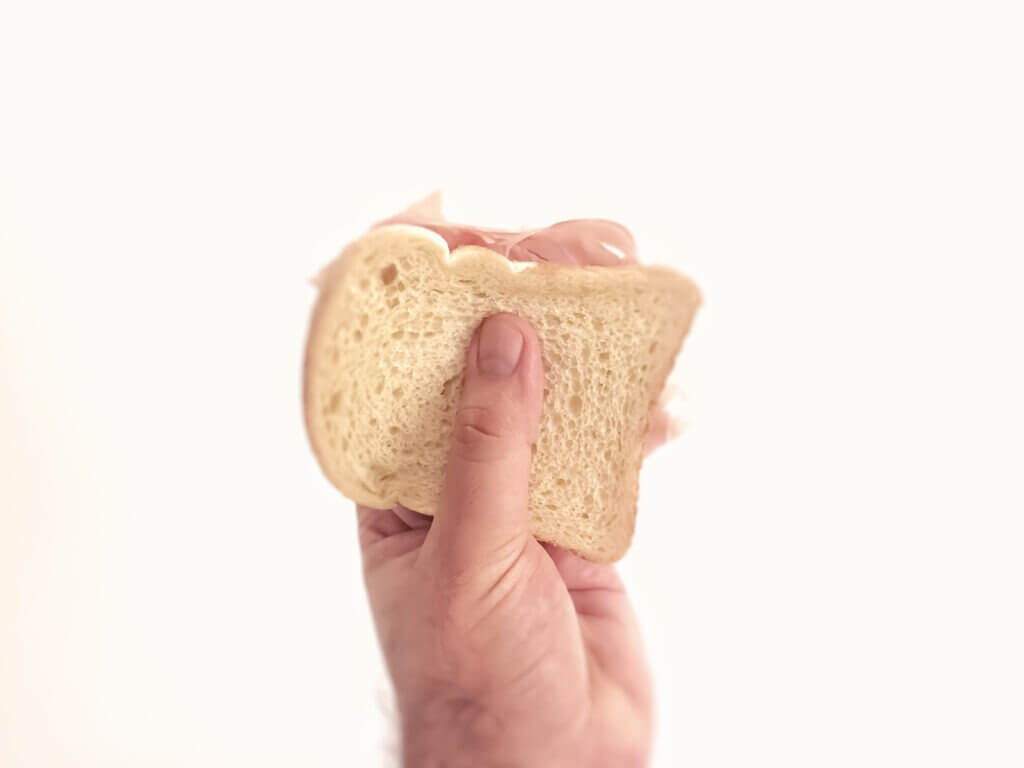 Male hand holding a baked ham sandwich