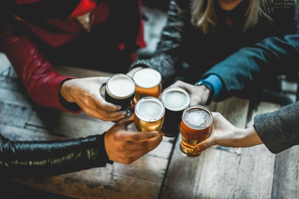 Young group of people having fun cheering with beer outdoor at bar restaurant - Soft focus on right hand holding glass