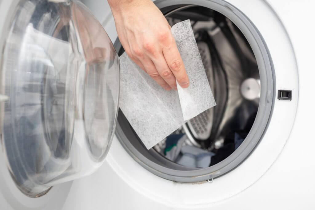 A hand dropping dryer aromatic sheets in a washing machine