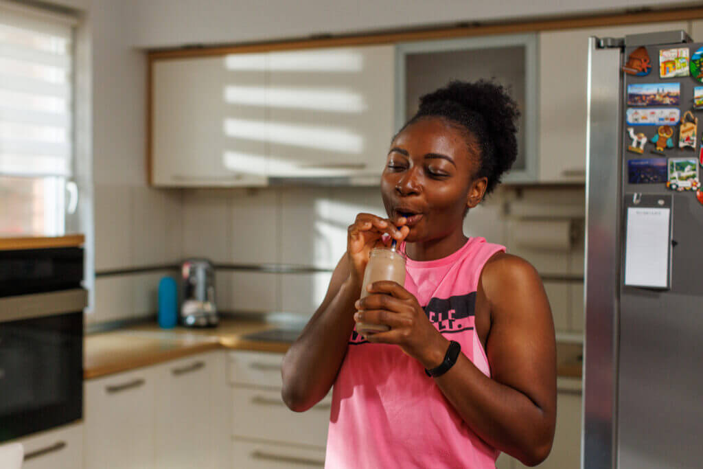 A young black woman enjoys in chocolate grass-fed protein shake at home.