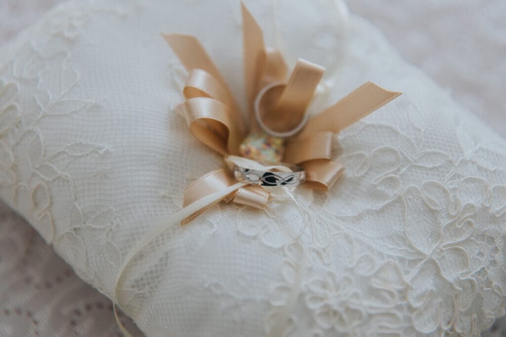 An elegant antique white ring pillow tied securely with lace ribbons to a crisp white sheet