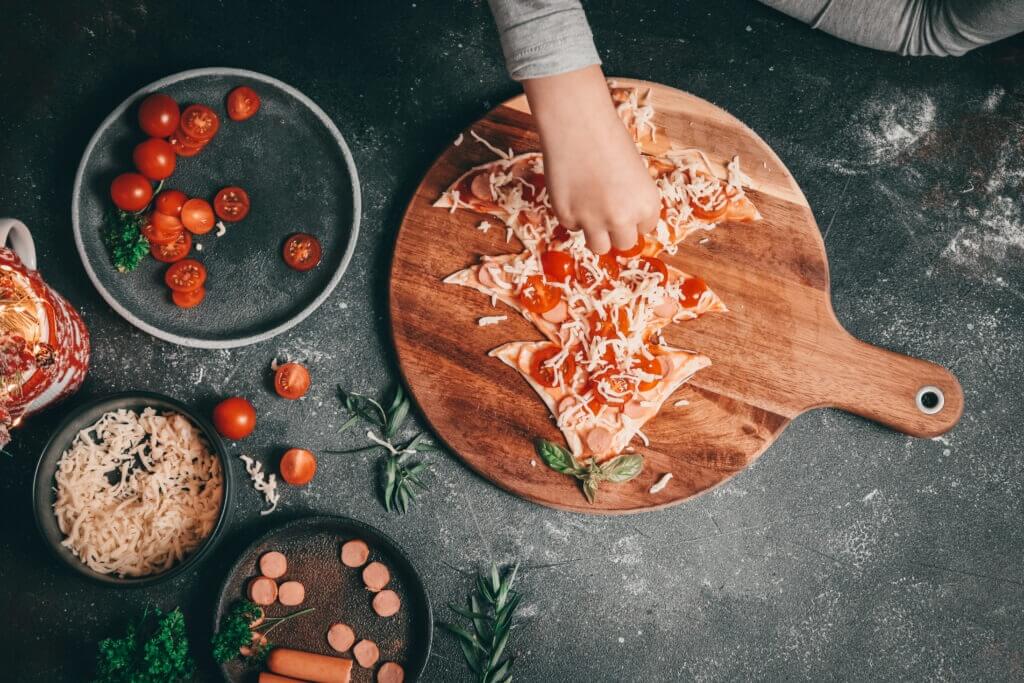 Children hand sprinkles mozzarella cheese on a pizza