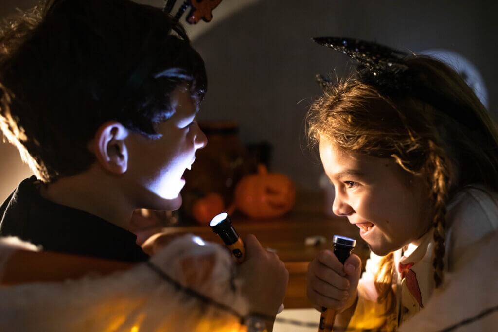 Kids are making scary faces with flashlights at home on Halloween