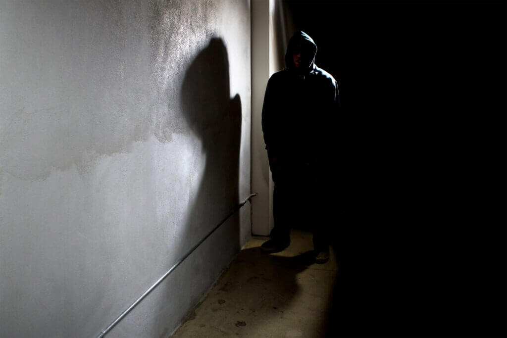 Photo of a hooded criminal stalking in the shadows of a dark street alley.