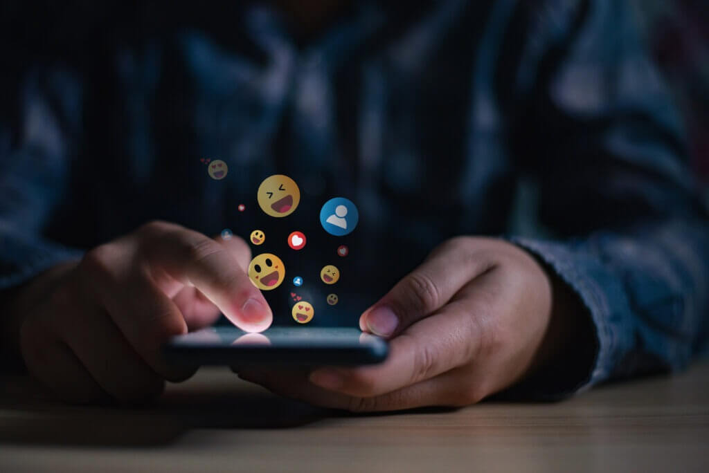 Young man using smartphone sending emojis, diverse positive emoji coming out of mobile phone.