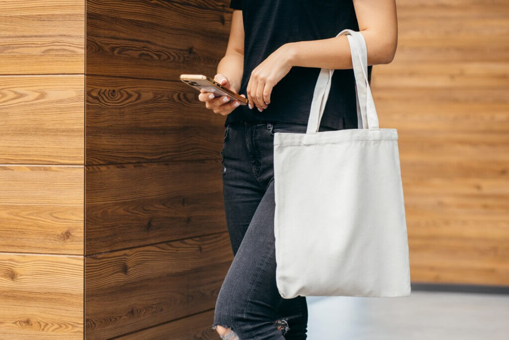 Young model girl on the street holding tote bag and mobile phone