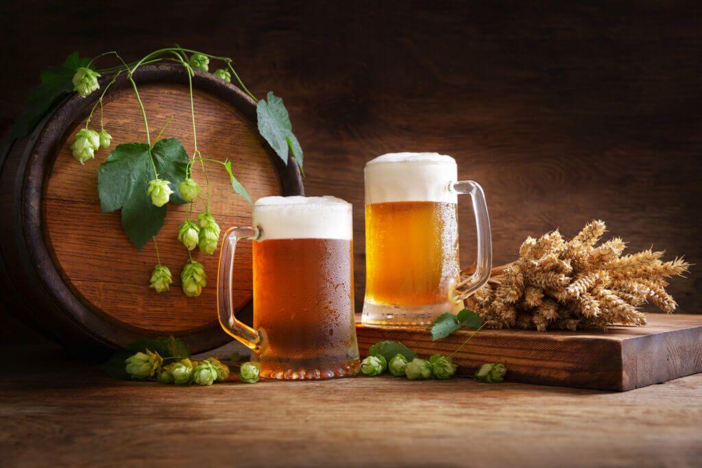 mug of beer, wheat ears, green hops and beer barrel on a wooden background