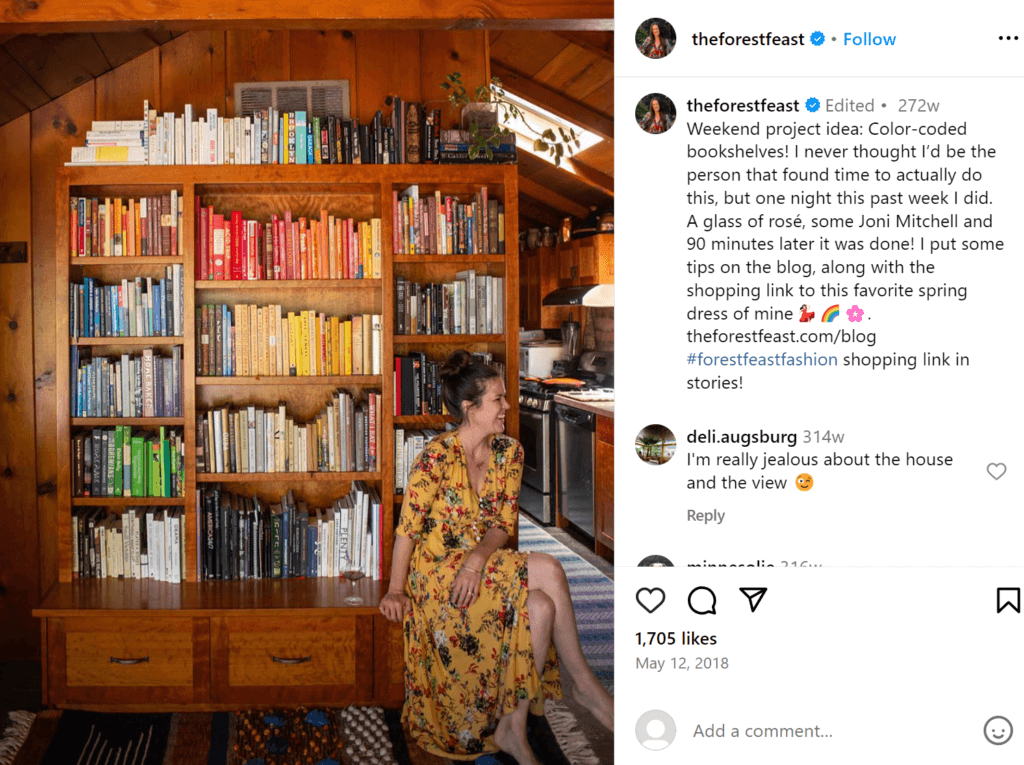 Colorful wooden shelf full of books organized by color, with a woman smiling seated on the floor in front.