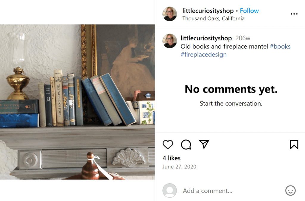 Muted blue books on a gray fireplace mantel piece, underneath an old-fashioned oil lamp with a framed antique portrait above. 