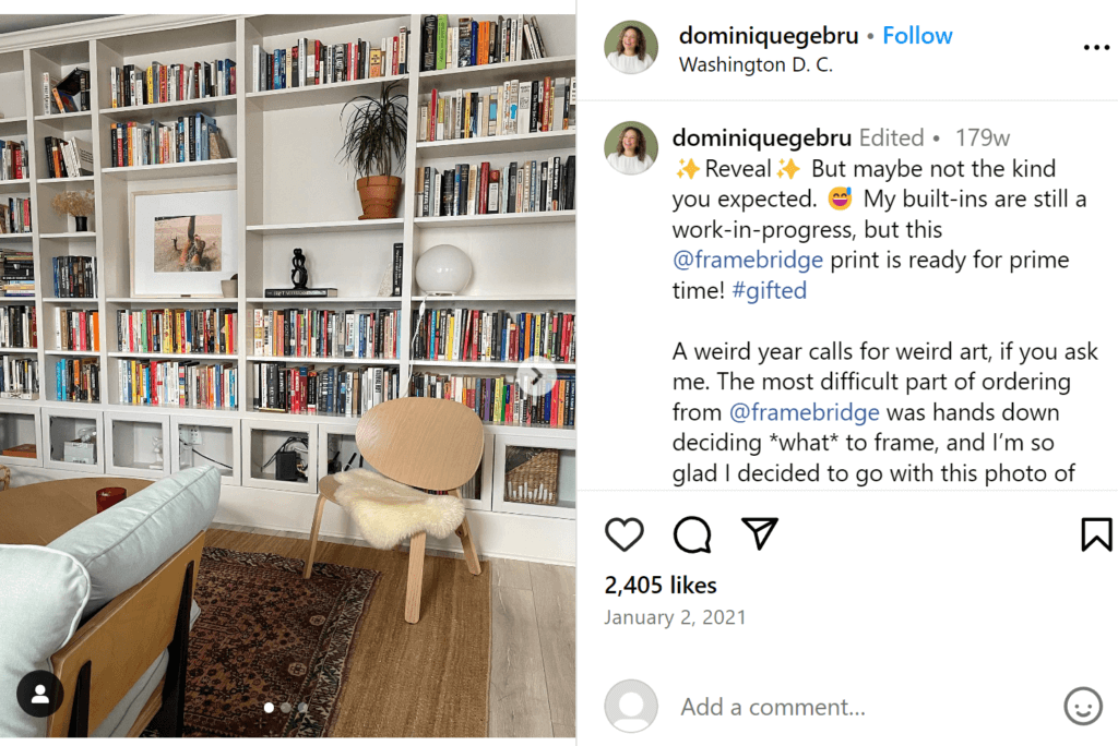 A full wall filled with modular book shelves, filled with colorful books in no particular order, as well as a plant, a framed photo, and some sculptures.