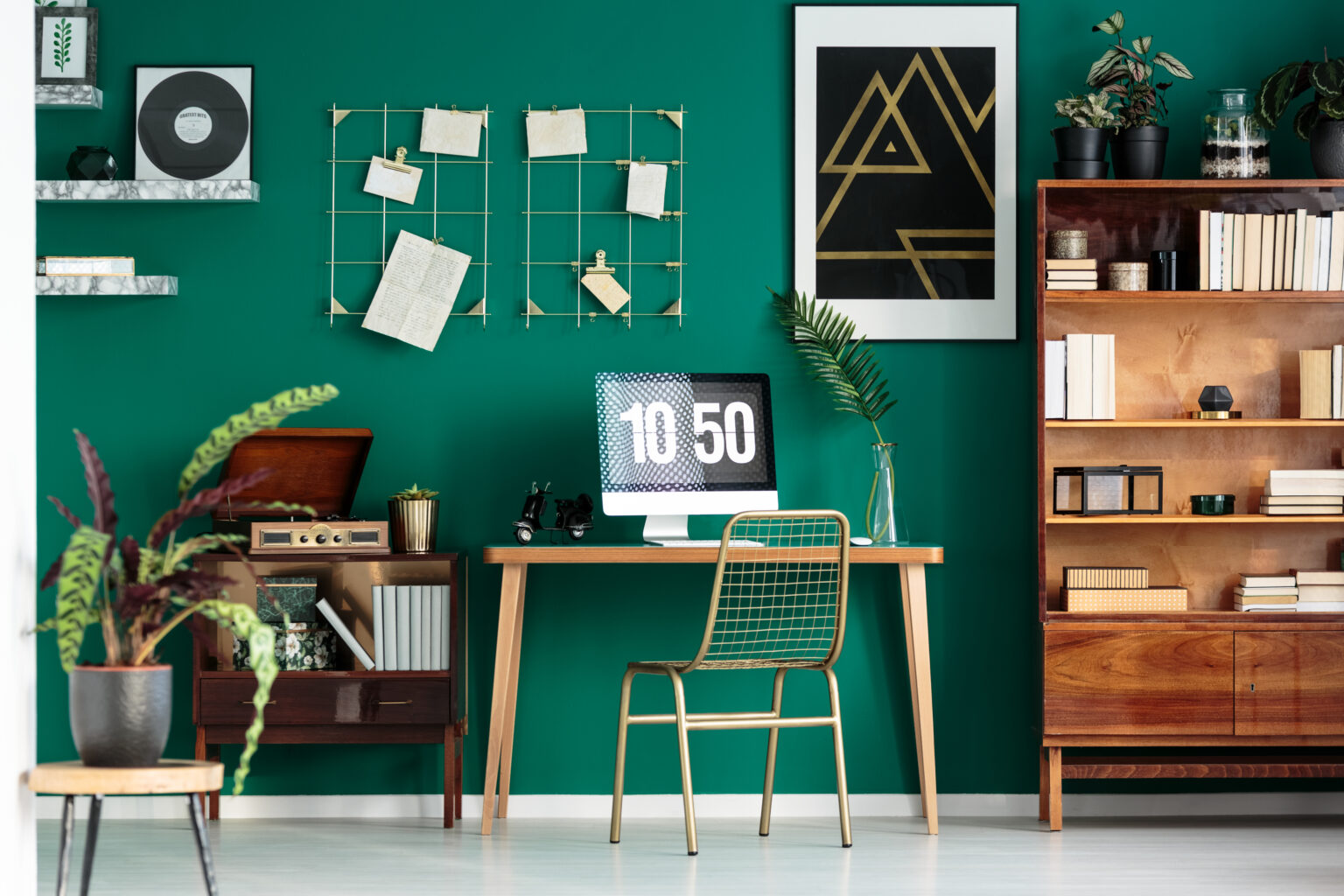 Home office and study corner with wooden desk and computer in green room interior with plants and poster