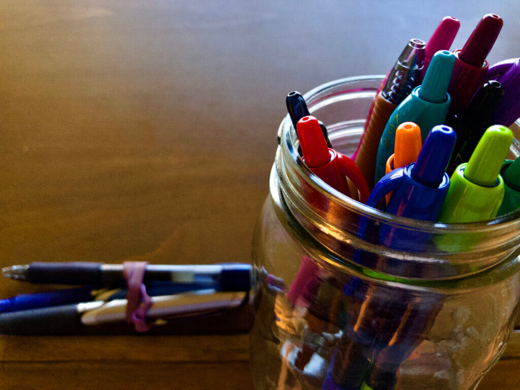 Glass jar holding colorful pens on wooden drafting table