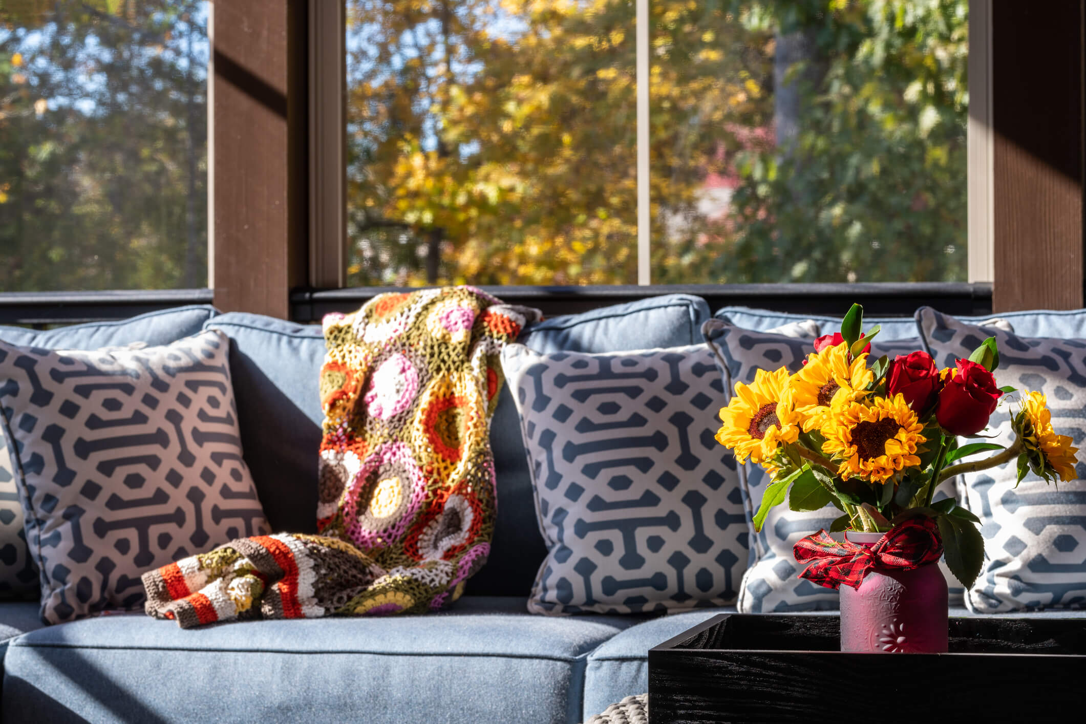 Cozy patio corner in a screened porch with flower bouquet in a vase, autumn leaves and woods in the background.