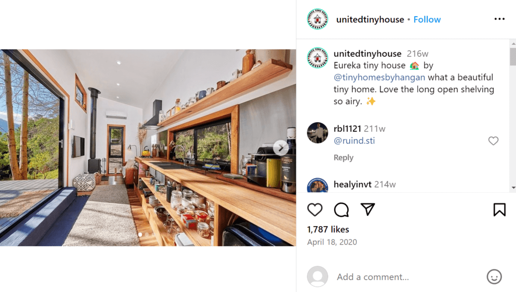 The long living space of a tiny home with open shelving lining one wall, acting as both storage and a countertop.