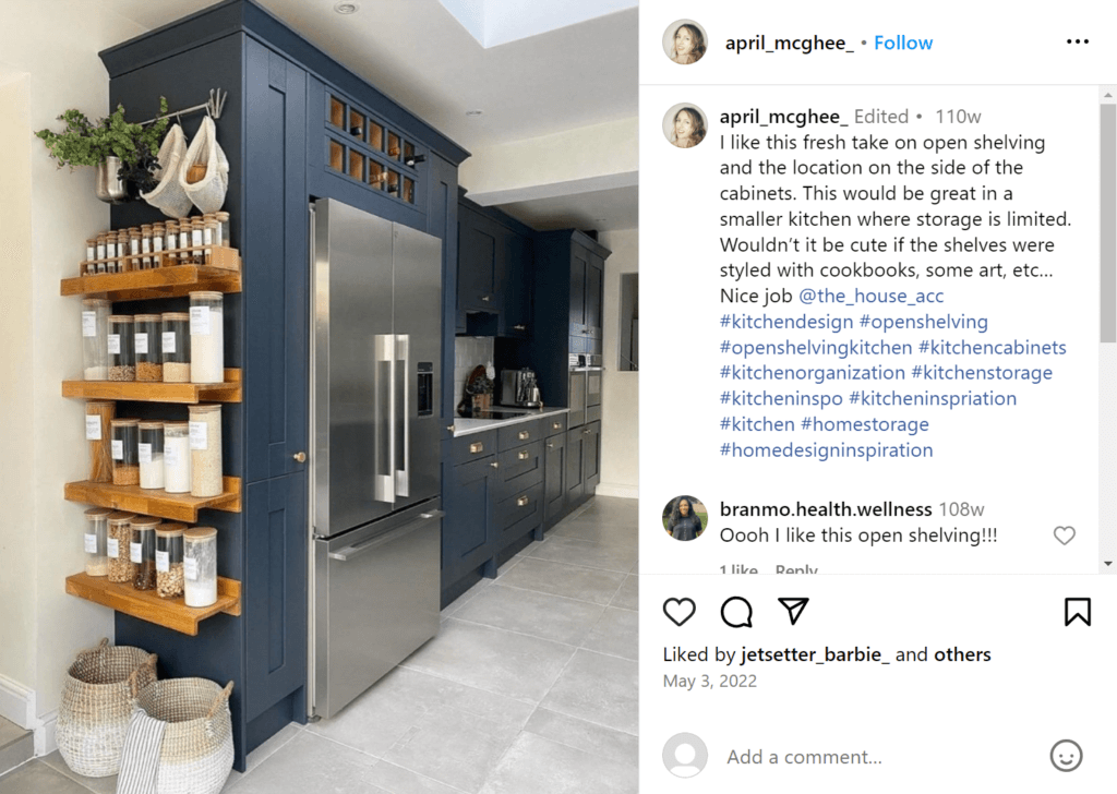 Beautiful kitchen with dark blue cabinets and refrigerator surround. On the side of the refrigerator surround facing towards the camera are open shelves with labeled canisters of spices and ingredients.