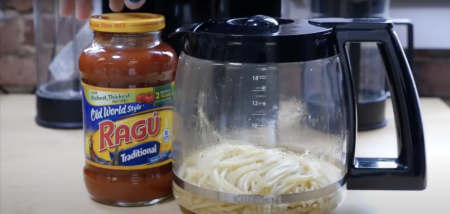 A jar of Ragu Old World Style Traditional pasta sauce next to a coffee pot containing cooked spaghetti noodles on a kitchen counter.