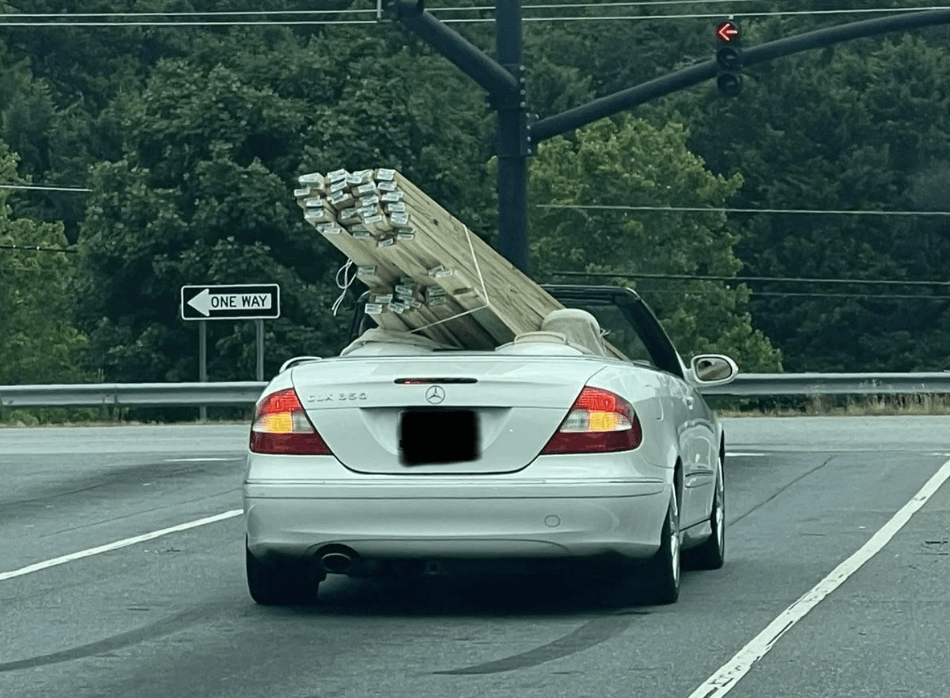 Small white convertible with wood planks hanging out the back