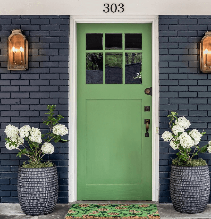 Fresh green door with decorative green doormat and potted plants on either side