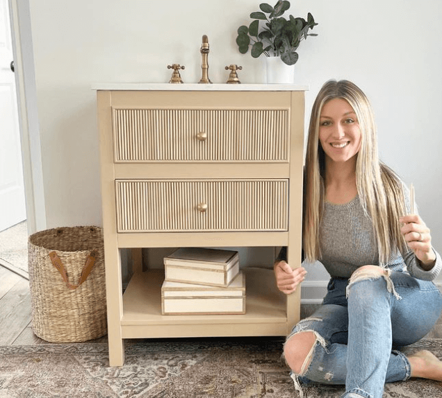 Woman sitting in front of a light beige bathroom vanity that has been DIYd with dowel rods