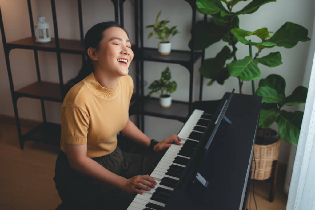 Asian woman learning to play the piano watching video clips from tablet, happy with relax time to learn about music.