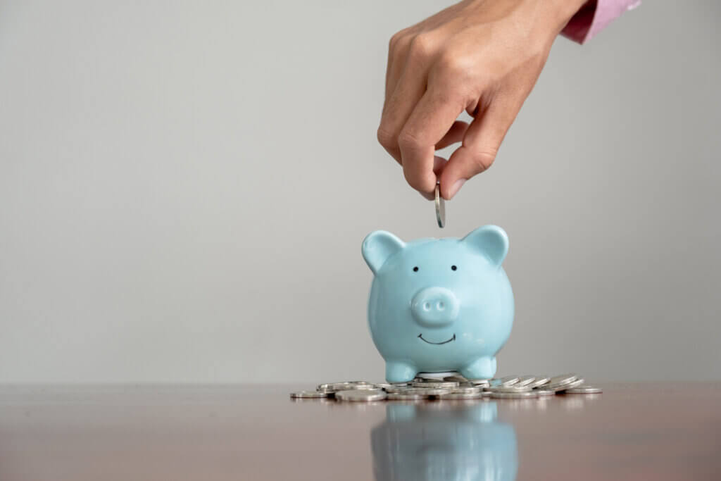 Businessman hand putting coin into blue piggy bank, step up start up business to success, Saving money for future plan and retirement fund concept