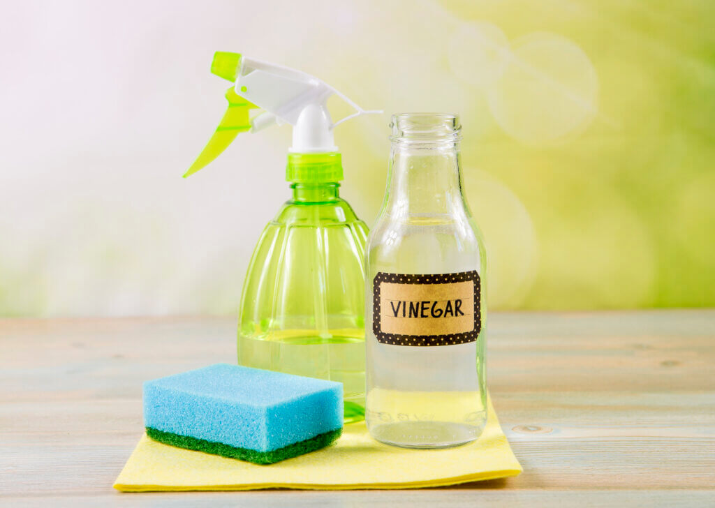 Chemical free home cleaner products concept. Using natural destilled white vinegar in spray bottle to remove stains. Tools on wooden table, green bokeh background, copy space.