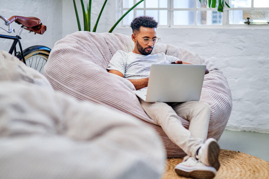 Full length shot of a handsome young businessman sitting on a beanbag alone in his office and using his laptop