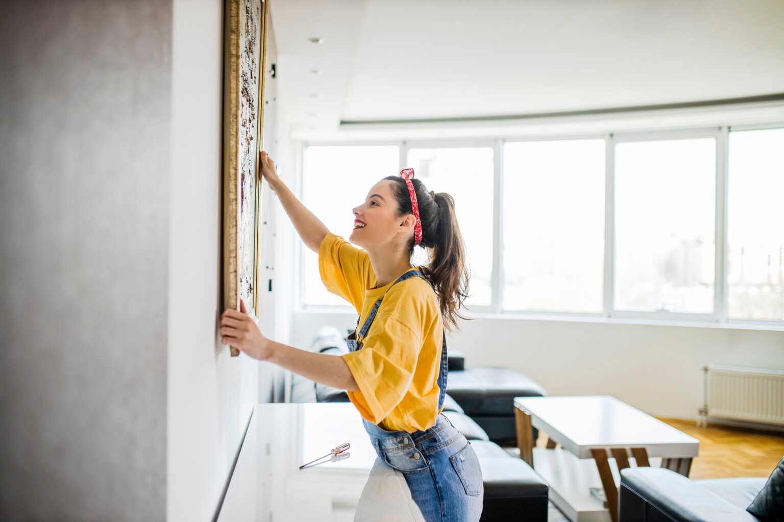 Young woman hanging a picture on a wall with a look of concentration