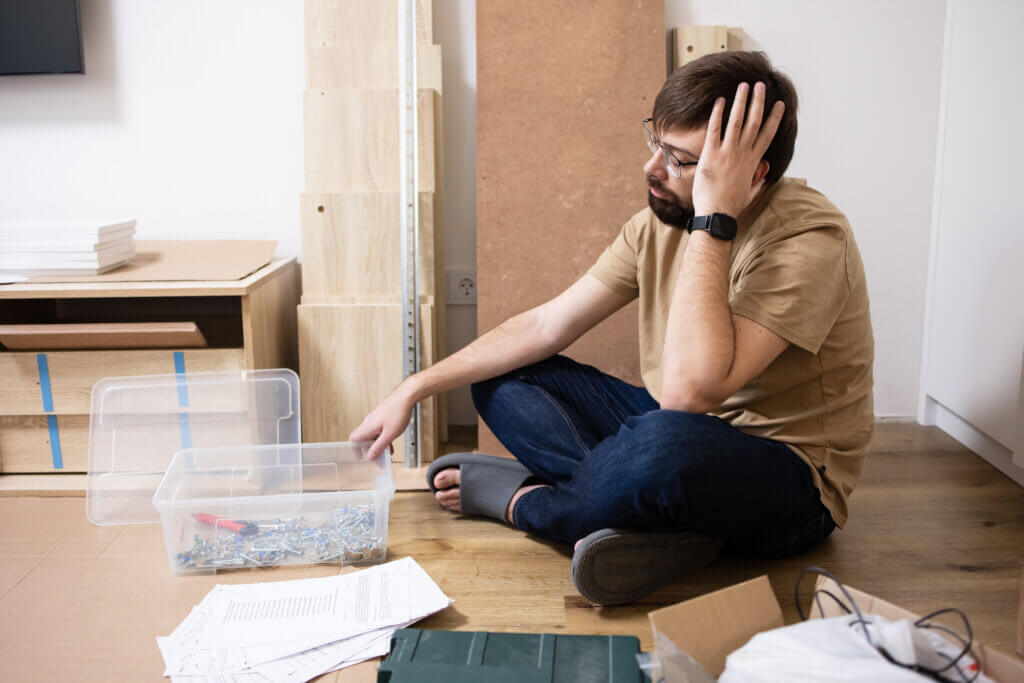 Difficult work, instructions and assembly of furniture. Frustrated confused man, reads instructions, goes crazy in the interior of the room with cabinet details, tools, instructions, screws and boxes