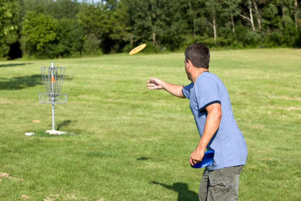 A man is playing a game of disk golf, throwing a yellow disk towards the basket