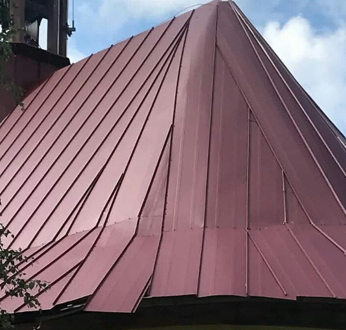 A red metal roof with uneven and poorly aligned panels, creating an irregular and unsightly appearance. The mismatched seams and varying panel lengths indicate a lack of precision and craftsmanship in the installation.