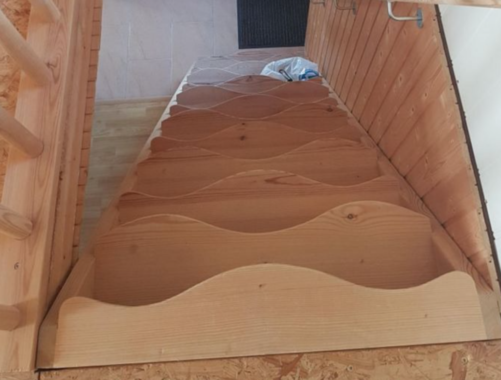 A wooden staircase with wavy, irregular steps that create an uneven surface, making it difficult and potentially unsafe to walk on. The design is visually striking but impractical for regular use.