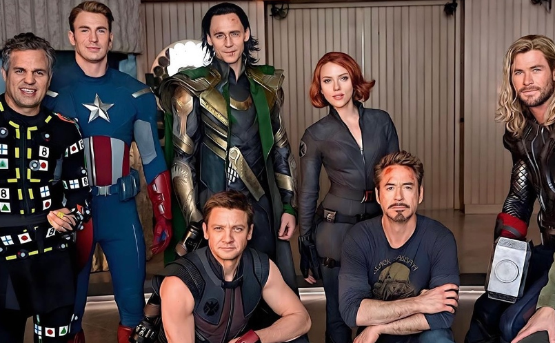 The cast of "The Avengers" in costume: Mark Ruffalo as Bruce Banner, Chris Evans as Captain America, Tom Hiddleston as Loki, Scarlett Johansson as Black Widow, Chris Hemsworth as Thor, Jeremy Renner as Hawkeye, and Robert Downey Jr. as Tony Stark. They are posing together in a relaxed setting.