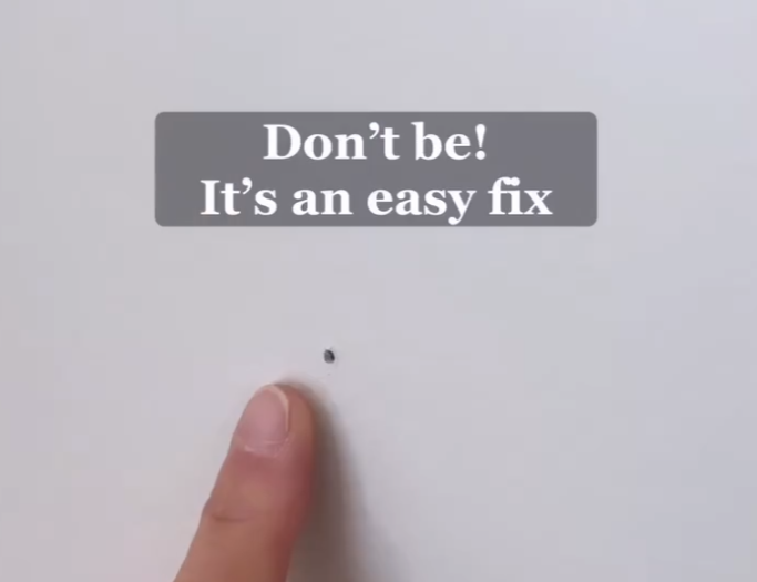 A finger points at a small hole in a wall, with a text overlay that reads, "Don’t be! It’s an easy fix." The image suggests a simple solution for repairing minor wall damage.