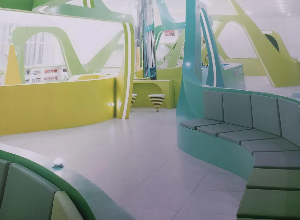 A futuristic, modern interior space characterized by smooth, curving lines and a palette of pastel greens and yellows. The design features modular seating arrangements with cushioned benches, abstract structural elements, and integrated lighting. The area has an open, airy feel, reminiscent of early 2000s visions of futuristic architecture, creating a unique and innovative ambiance.