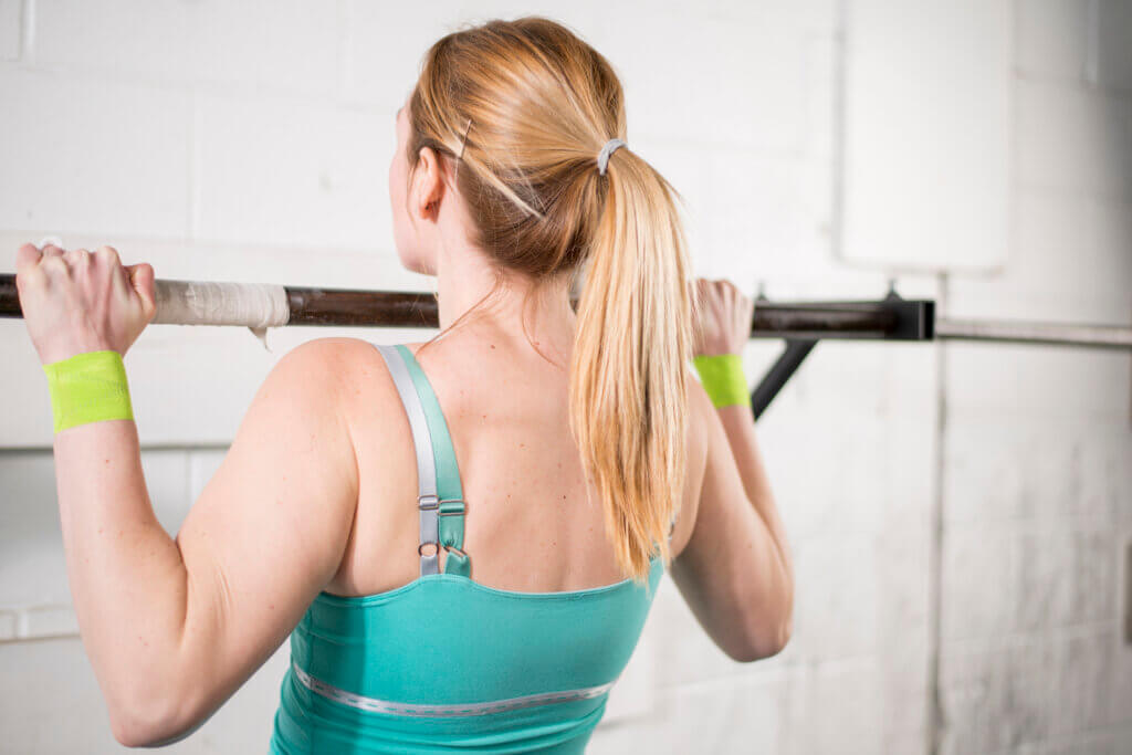 A woman is doing pull ups on a bar at the gym.