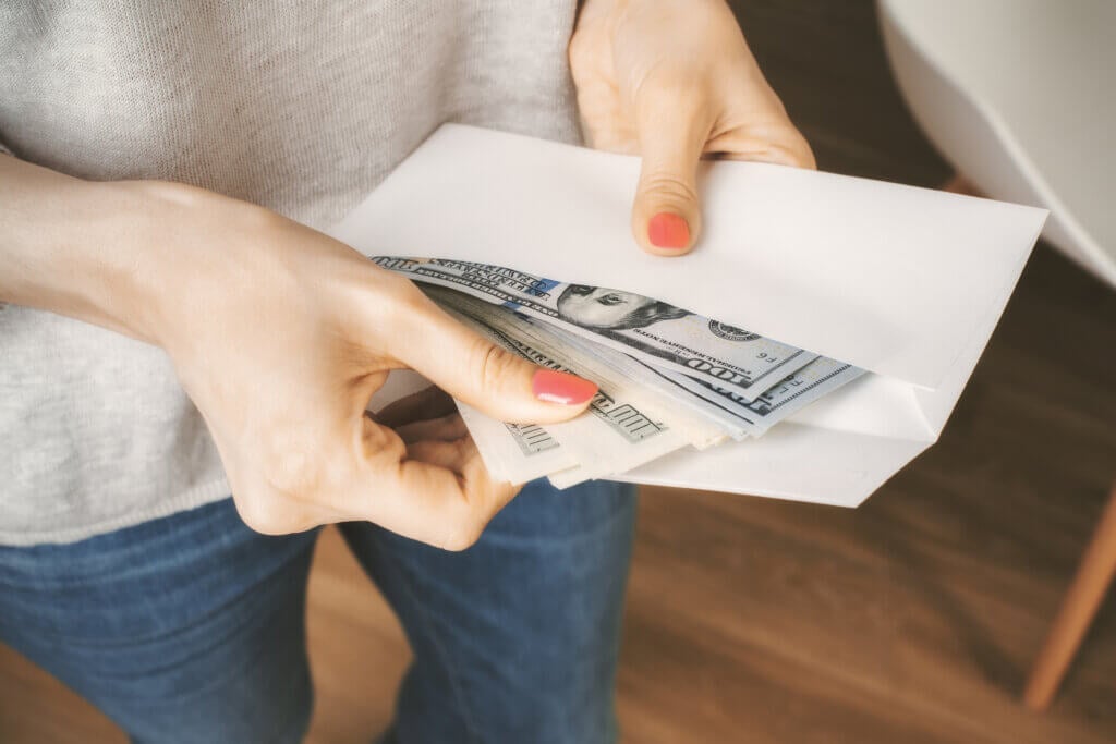 Woman in jeans and grey top holding envelope with cash. Concept of corruption and bribery