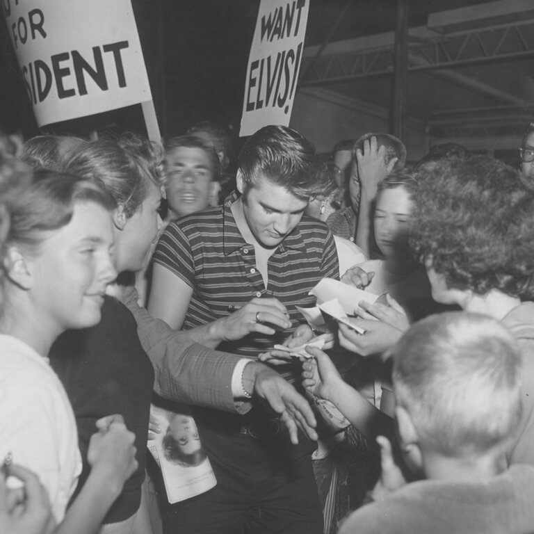 Elvis Presley surrounded by fans signing autographs