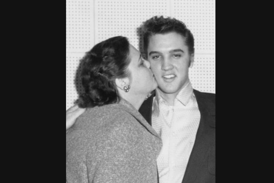 A midlle age woman, Elvis Presley's mother, kissing him on the cheek while he smiles and looks directly at the camera