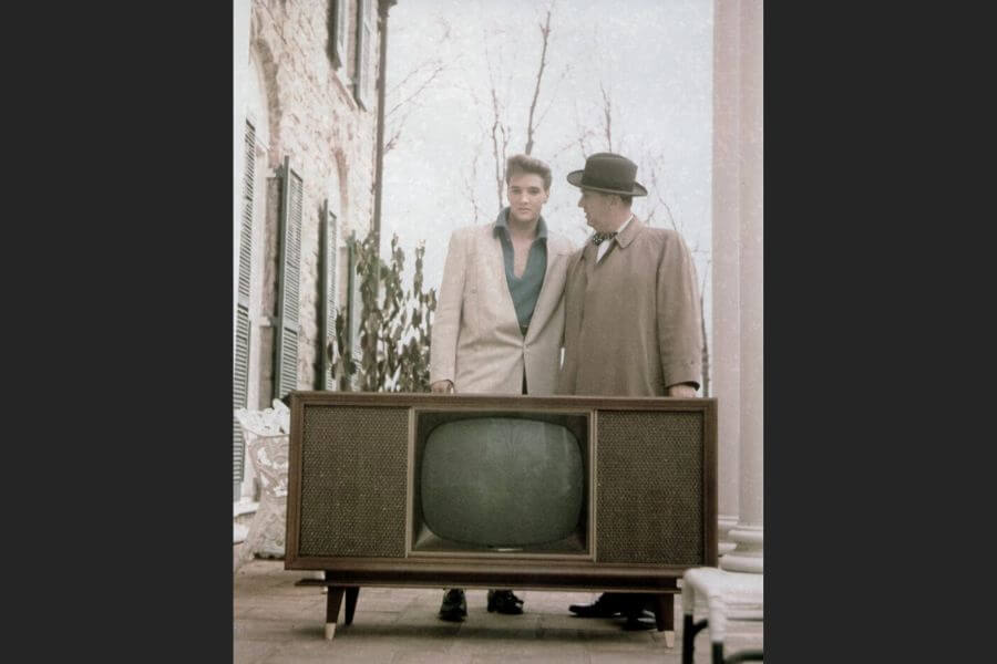 Elvis and his manager looking at a huge tv in the 1950s