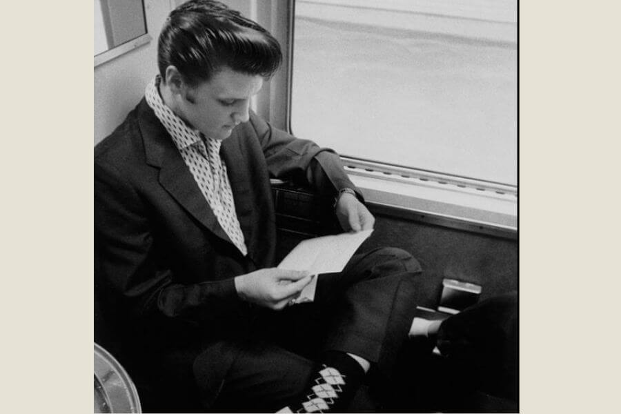 Elvis reading a letter while sitting on a train