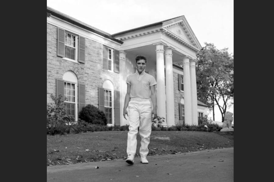 A young Elvis Presley standing in front of his Graceland Mansion