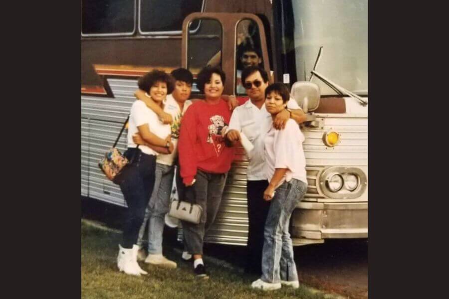 A young Selena Quintanilla standing in front otf a bus with family members. 