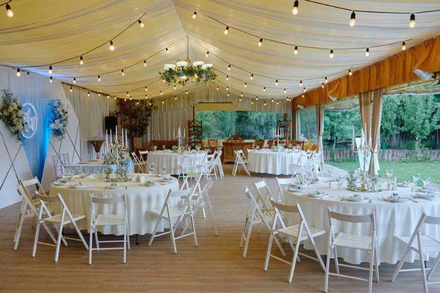 Table setting with sparkling wineglasses and cutlery on table, copy space. Place setting at luxury wedding reception. Round table and white wood chairs served for wedding banquet in restaurant
