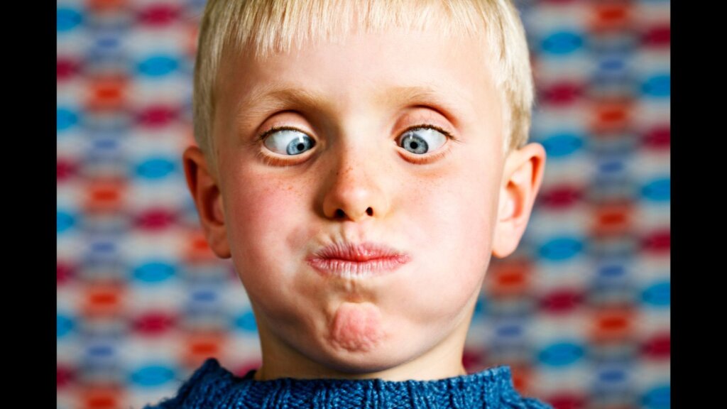 Blond boy is crossing his eyes and blowing out his cheeks as he looks down at his possibly very full mouth!