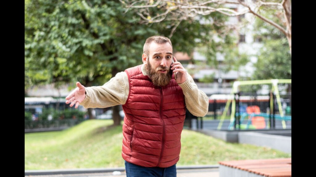 Young angry man shouting out talking on phone outdoors.