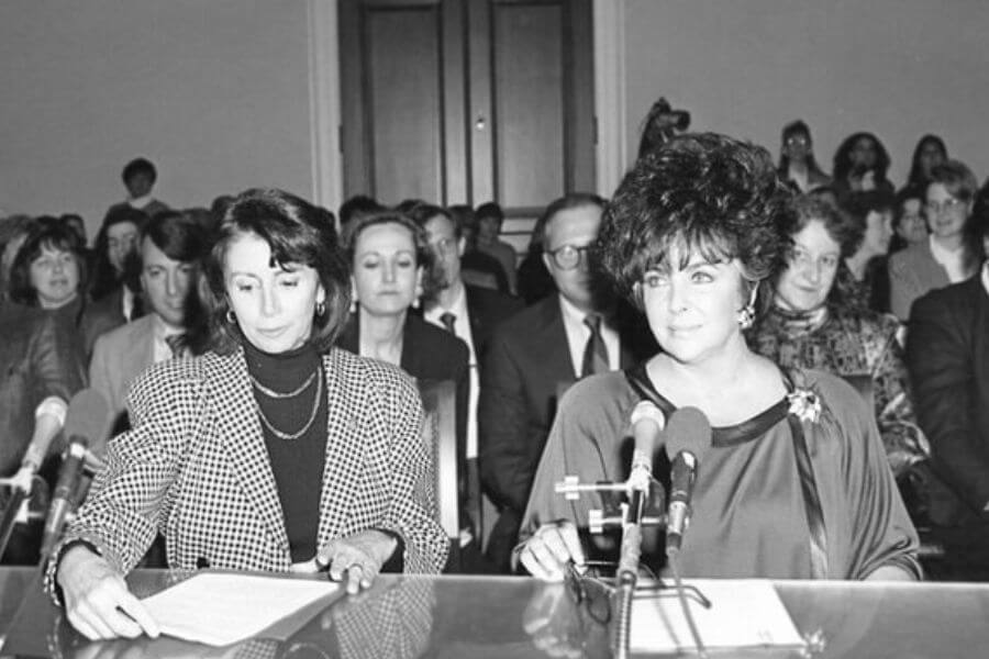 Nancy Pelosi and Elizabeth Taylor sitting in front of a desk