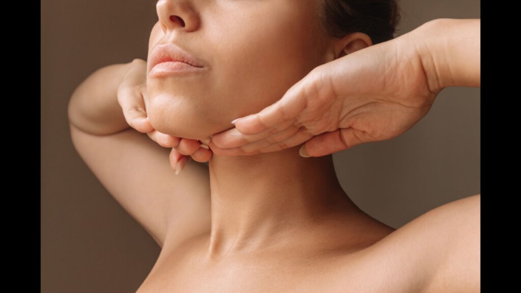 Woman touching under the chin with hands massaging her face on dark brown background.