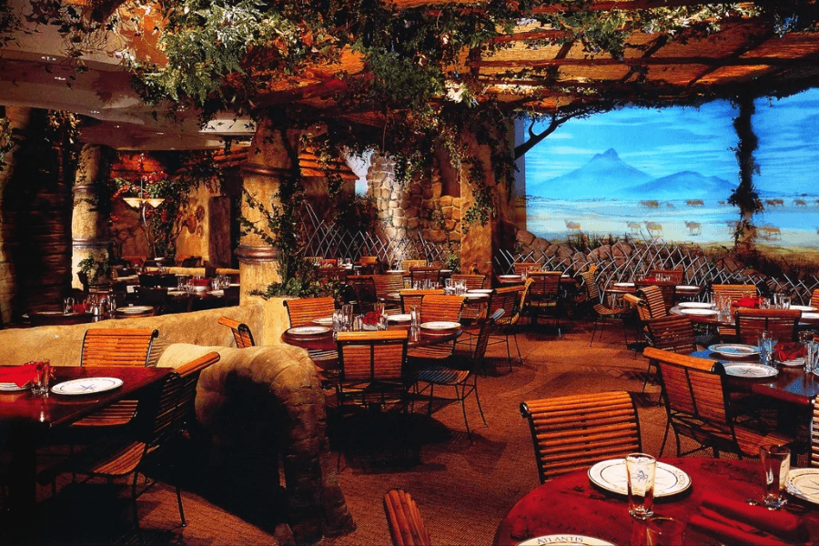 The image features a beautifully themed restaurant interior resembling a lush, jungle-like environment with vines, stone columns, and scenic wall art, creating an immersive dining experience reminiscent of a tropical or exotic escape.